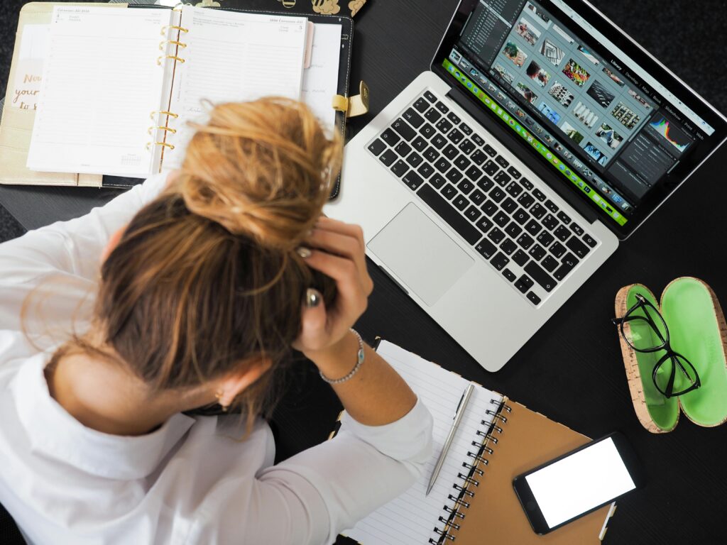 Home Overhead view of a stressed woman working at a desk with a laptop, phone, and notebooks.